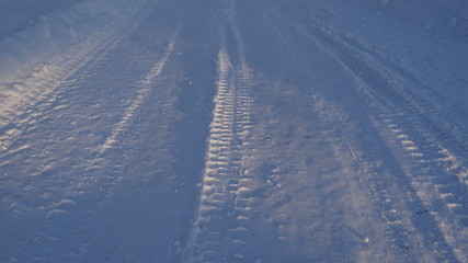 Traces of heavy machinery on a snowy road in the rays of the rising sun.