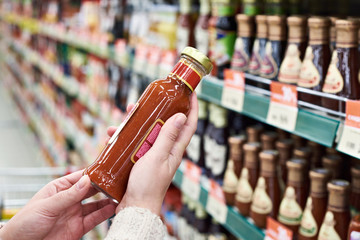 Buyer hands with bottle of chilli sauce in store