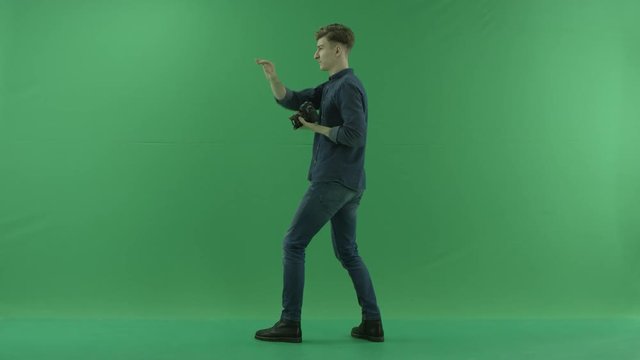 Photographer taking photos on the left hand side back to the viewer on the green screen and corrects standing of a model
