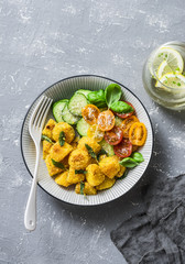 Crispy baked slices of polenta with sage butter and vegetables cucumbers, tomatoes, basil salad on a gray background, top view. Vegetarian food © okkijan2010