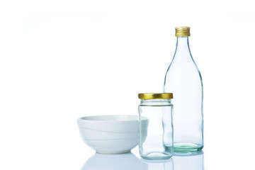Empty clear glass bottles in various sizes and shapes with lids and a white ceramic bowl on white