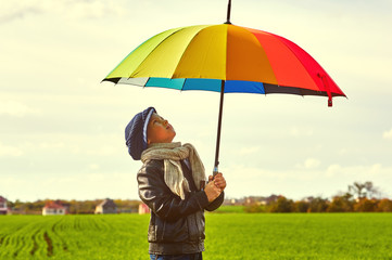 Boy on the field with a bright colorful umbrella . The child enjoys nature
