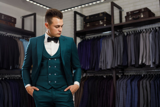 young man in classic vest against row of suits in shop