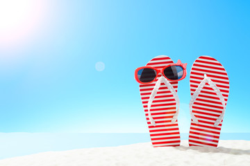 Red striped flip flops and sunglasses on sandy beach