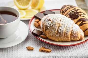 Fresh baked croissants with chocolate for breakfast, a cup of tea, lemon, almonds
