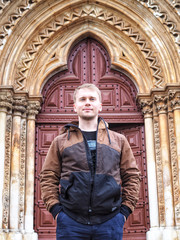 Obraz premium A man in a jacket stand against huge antique doors, man on the background of old doors