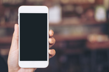 Mockup image of a hand holding white mobile phone with blank black desktop screen with blur background