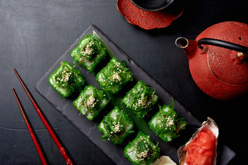 Green sushi set with chuka served on black clay plate with soy sauce and chopsticks, top view. Delicious traditional Japanese food, sushi restaurant concept