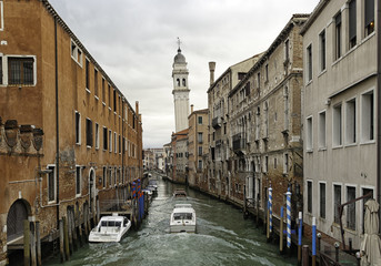 View from a bridge of a typical water canal in the Venetian lagoon with old buildings on the sides. One of the famous canals in Venice with poles and boats