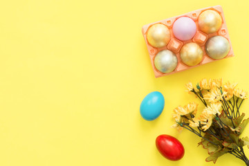 Flat lay top view colorful easter egg painted in pastel colors composition and spring flowers on yellow pastel color background. Easter day background top view with copy space.