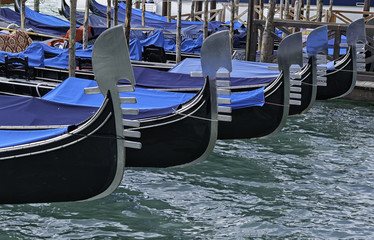 Obraz premium Detail on the steel prow of a Venetian gondola moored in the canal in front of San Marco square in Venice. The gondola is a traditional flat-bottomed boat similar to a canoe. Unesco