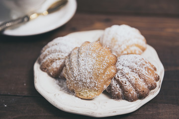 Homemade french madeleines with beurre noisette and cup of coffee on wooden table. Horizontal.