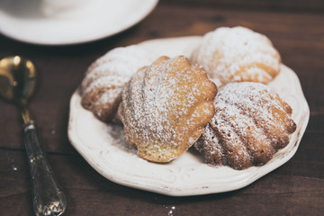 Homemade french madeleines with beurre noisette and cup of coffee on wooden table. Horizontal.