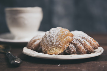Homemade french madeleines with beurre noisette and cup of coffee on wooden table. Horizontal.
