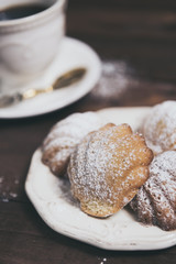 Homemade french madeleines with beurre noisette and cup of coffee on wooden table. Vertical. Close-up.
