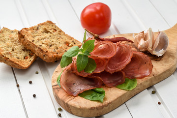Salami smoked sausage slices basil leaves and peppercorns on white background