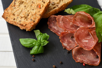 Salami smoked sausage slices basil leaves and peppercorns on bla