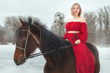 Young woman in red dress riding horse.