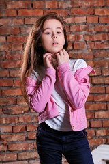 Fototapeta na wymiar Stylish teen girl posing at studio front Brick wall background. Fashion portrait young caucasian child model. Attractive hipster girl touching face,looking at camera sensually,confidently.