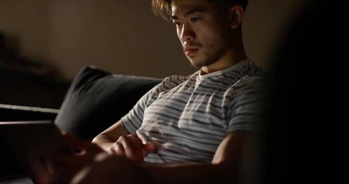 4K Serious young man working late at home with computer tablet