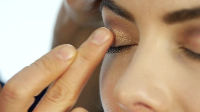 makeup artist applies a corrector under his eyes, makeup for pretty woman in beauty salon