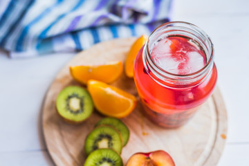 Red fruit lemonade with ice in a jar and fresh tropical fruits on a wooden tray - top view