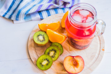Red fruit lemonade with ice in a jar and fresh tropical fruits on a wooden tray - top view