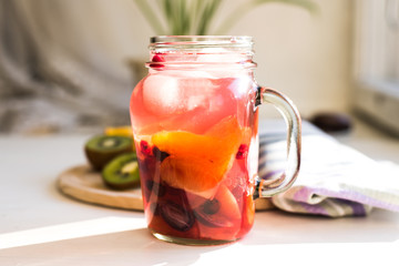 Red fruit homemade lemonade with ice in a jar in the morning in the sun