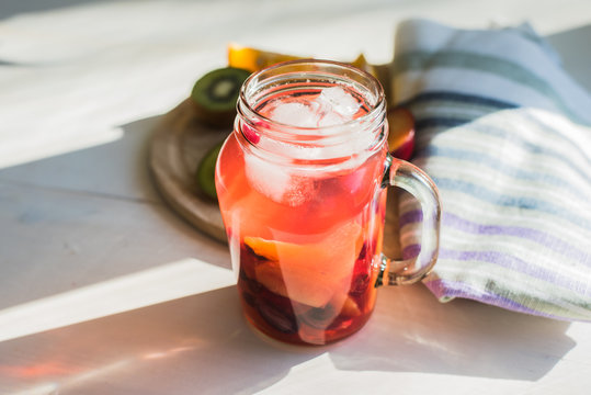 Red fruit homemade lemonade with ice in a jar in the morning in the sun