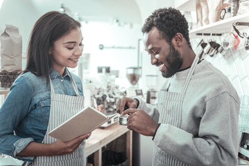 Fototapeta premium At the coffee shop. Delighted nice positive woman holding a notebook and looking at her colleague while working together in the coffee shop