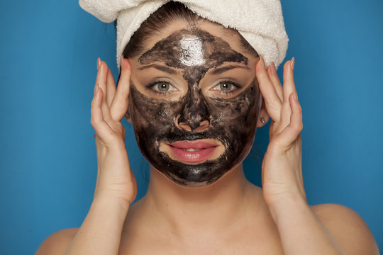 Young happy woman with towel on her head posing with black mask on her face