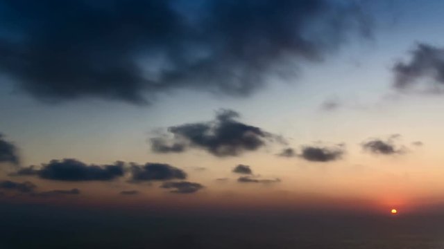 	 4k time lapse of clouds crossing the amazing sky over the sea or ocean at sunset. transition from day to night. The clouds cross slowly from left to right colored yellow orange purple blue.