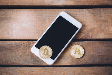 Two coins of Crypto currency Bitcoin with smart phone with copy space over wooden background. Cryptocurrency and future of digital financial banking trade