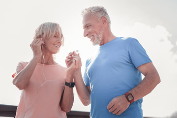 Try this. Satisfied aged pleasant woman standing on the street smiling and headphone to a man.