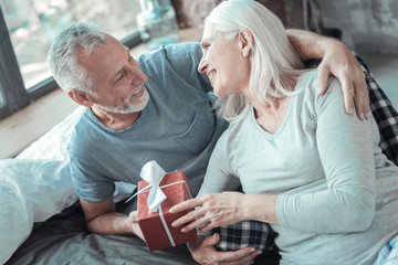 Love you so much. Lovely senior cute couple lying on the bed together smiling and holding the present.