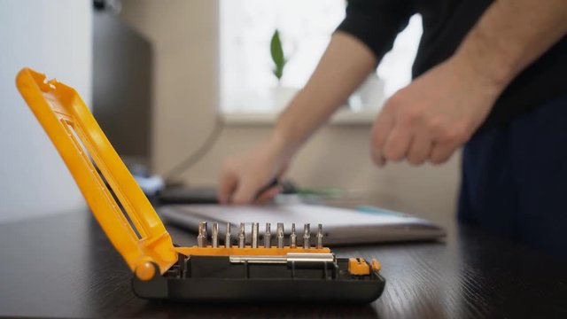 The wizard uses a screwdriver to twist the screw on the lid of the notebook.