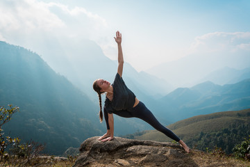 Woman doing yoga on mountain cliff at sunrise. Mountanious landscape