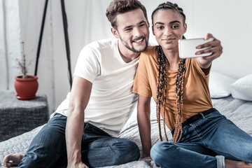 Our photo. Happy cheerful delighted couple sitting on the bed and taking a selfie while enjoying their time together