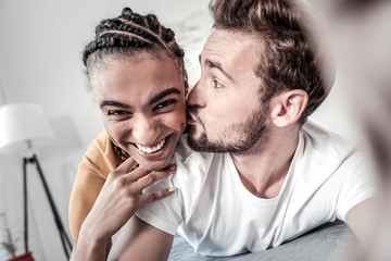 Fototapeta premium Expression of love. Happy bearded young man looking at his girlfriend and kissing her in the cheek while expressing his love