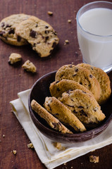 Chocolate chip cookies in a bowl on wooden table with glass of milk
