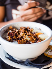Eating healthy breakfast bowl. Yogurt, granola, seeds, fresh and dry fruits woman' s hands at background. Clean eating, dieting, detox, vegetarian food concept
