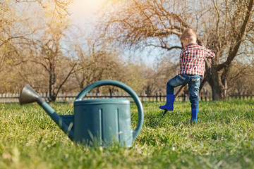 Like doing it. Pleasant little boy holding a shovel and digging the soil while watering can standing in the foreground