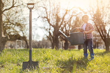 Helpful gardening tools. Selective focus of a shovel in the ground with a nice little boy watering the grass in the backgroud