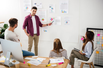 marketing manager pointing at white board with papers on business meeting with multiethnic...