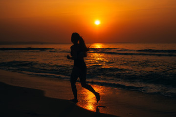 Fototapeta na wymiar girl running against orange sunrise by the sea on the beach