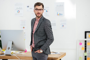 portrait of young businessman in suit and eyeglasses looking at camera at workplace in office