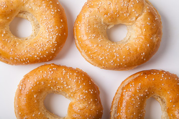 Four fresh baked bagle buns with sesame seeds on white background pre-cut for making sandwiches