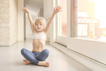 Fototapeta na wymiar Little blond girl doing a yoga exercise in the sunny room