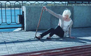 Oh no. Frightened retired woman leaning on a walking cane while trying to stand up after falling to...