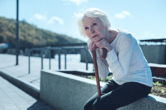 When I Was Young. Pensive Elderly Woman Sitting Outside With Her Hands And Chin On A Walking Cane And Looking Into Vacancy While Remembering Her Past.